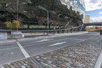 an empty road with a bricked sidewalk in front of an opera building with reflective windows