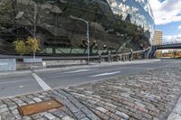 an empty road with a bricked sidewalk in front of an opera building with reflective windows