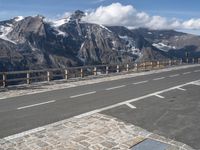 an empty road going over a mountain range with snow covered mountains in the background with white markings