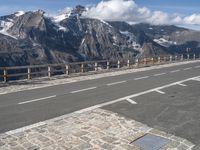 an empty road going over a mountain range with snow covered mountains in the background with white markings