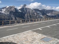 an empty road going over a mountain range with snow covered mountains in the background with white markings