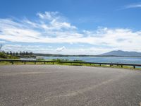 an empty road that looks down on the water and the beach with mountains in the distance