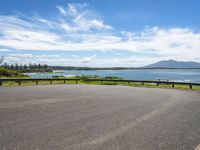 an empty road that looks down on the water and the beach with mountains in the distance