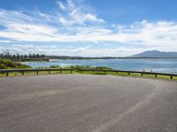 an empty road that looks down on the water and the beach with mountains in the distance