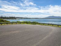 an empty road that looks down on the water and the beach with mountains in the distance