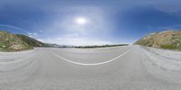 a 360 - panorama image shows an empty road with a sunny blue sky in the background