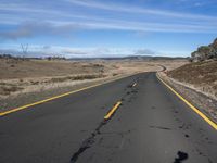 an empty road on the side of a hill near a yellow fencepost and dirt road