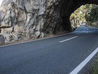 an empty road goes into a rock cave as it is closed to traffic and people walk