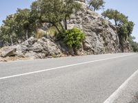 an empty road is near some rock formations and some trees and bushes are on the side of the road