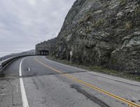 the road is empty and has some rock formations along it with yellow arrows running on it