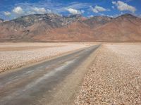 the mountain range is lined with rocks and gravel near a empty road with people walking on it