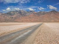 the mountain range is lined with rocks and gravel near a empty road with people walking on it