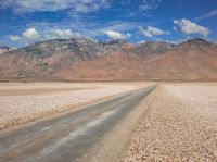 the mountain range is lined with rocks and gravel near a empty road with people walking on it