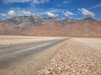 the mountain range is lined with rocks and gravel near a empty road with people walking on it