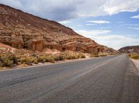 the empty road is surrounded by rocky hills and bushes, as well as large rock formations