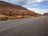 the empty road is surrounded by rocky hills and bushes, as well as large rock formations