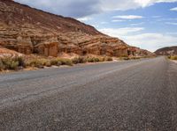 the empty road is surrounded by rocky hills and bushes, as well as large rock formations