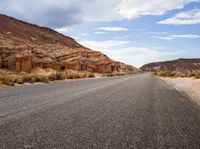 the empty road is surrounded by rocky hills and bushes, as well as large rock formations