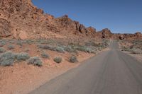 an empty road going through some rocky hills and desert in the background are sparse bushes