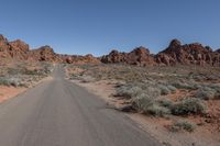 an empty road going through some rocky hills and desert in the background are sparse bushes
