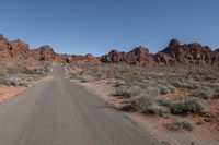 an empty road going through some rocky hills and desert in the background are sparse bushes