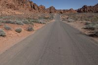 an empty road going through some rocky hills and desert in the background are sparse bushes