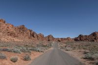 an empty road going through some rocky hills and desert in the background are sparse bushes