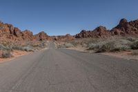 an empty road going through some rocky hills and desert in the background are sparse bushes