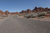 an empty road going through some rocky hills and desert in the background are sparse bushes