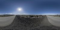 the view of an empty road and a dirt road next to a blue sky with a sun