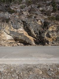 an empty road has rocky terrain and trees on the side of it and two motorcycles passing each other