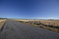 a empty road runs through an open grassy area to the horizon, as clouds above a fence