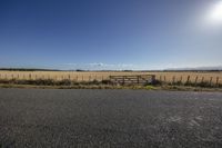 a empty road in an open field, with a fence and gate in the foreground