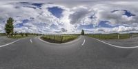 an empty road that has several different sides on it and clouds and blue sky behind