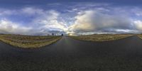 there is a large empty paved road with clouds in the sky above it and the ground below