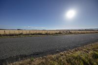 a long empty road sitting on top of a grass covered hillside next to a wooden fence