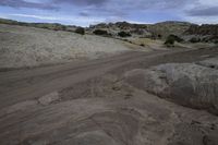 an empty road running through some dirt field near a rock formation and tree line in the distance