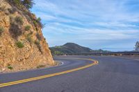 the empty road is passing by a very scenic cliff wall with steep inclines behind it