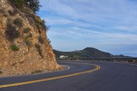 the empty road is passing by a very scenic cliff wall with steep inclines behind it