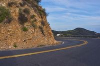 the empty road is passing by a very scenic cliff wall with steep inclines behind it