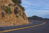 the empty road is passing by a very scenic cliff wall with steep inclines behind it