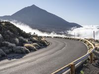 an empty road on the side of a mountain near the clouds and fogs behind it