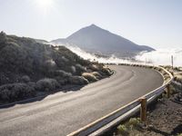 an empty road on the side of a mountain near the clouds and fogs behind it