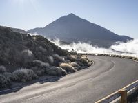 an empty road on the side of a mountain near the clouds and fogs behind it