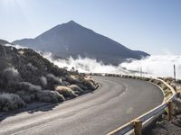 an empty road on the side of a mountain near the clouds and fogs behind it