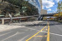 an empty road and sidewalk in front of a building with a massive glass front and walkway