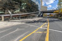 an empty road and sidewalk in front of a building with a massive glass front and walkway