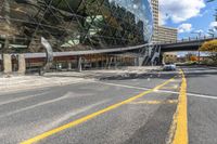 an empty road and sidewalk in front of a building with a massive glass front and walkway