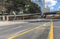 an empty road and sidewalk in front of a building with a massive glass front and walkway