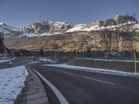 an empty road with snow on the ground and mountains in the background with traffic signs